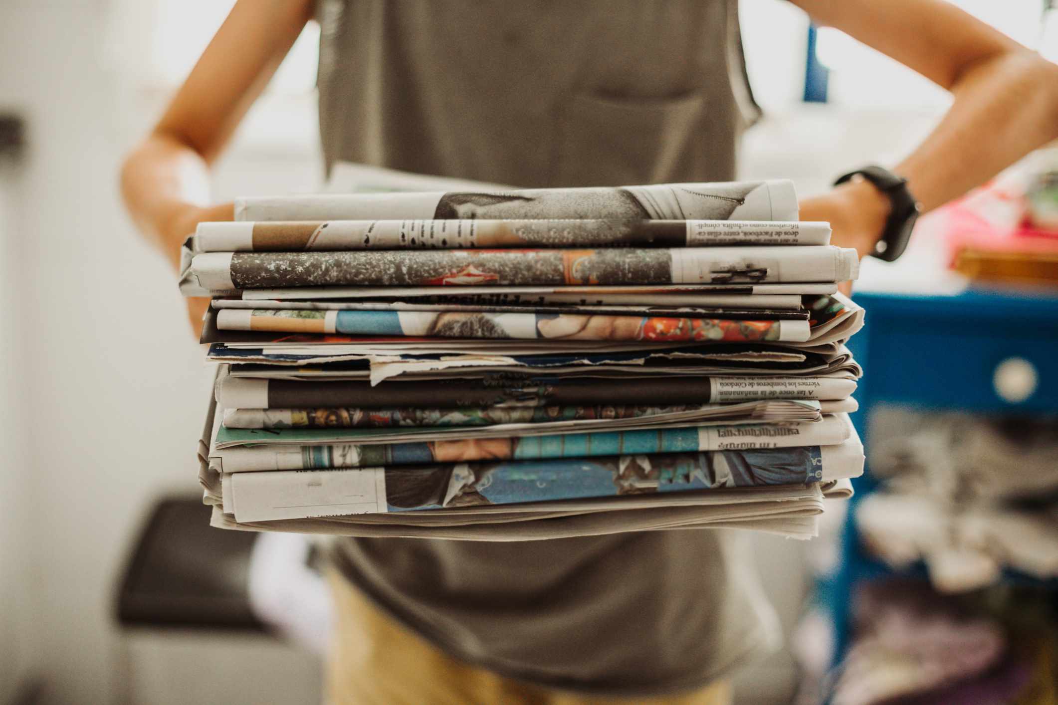 midsection of person holding a pile of newspapers