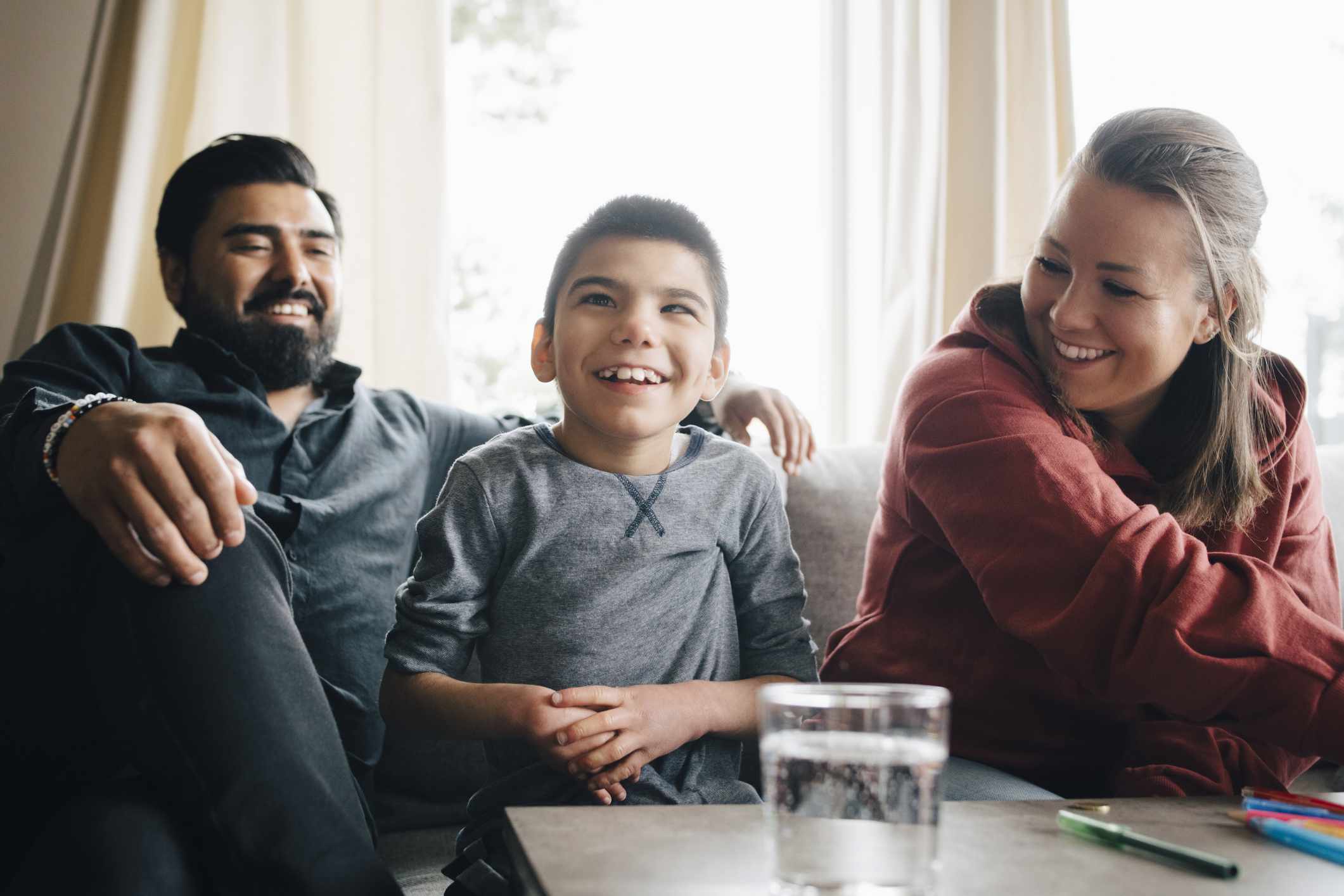 Smiling parents looking at autistic son while sitting on sofa in living room