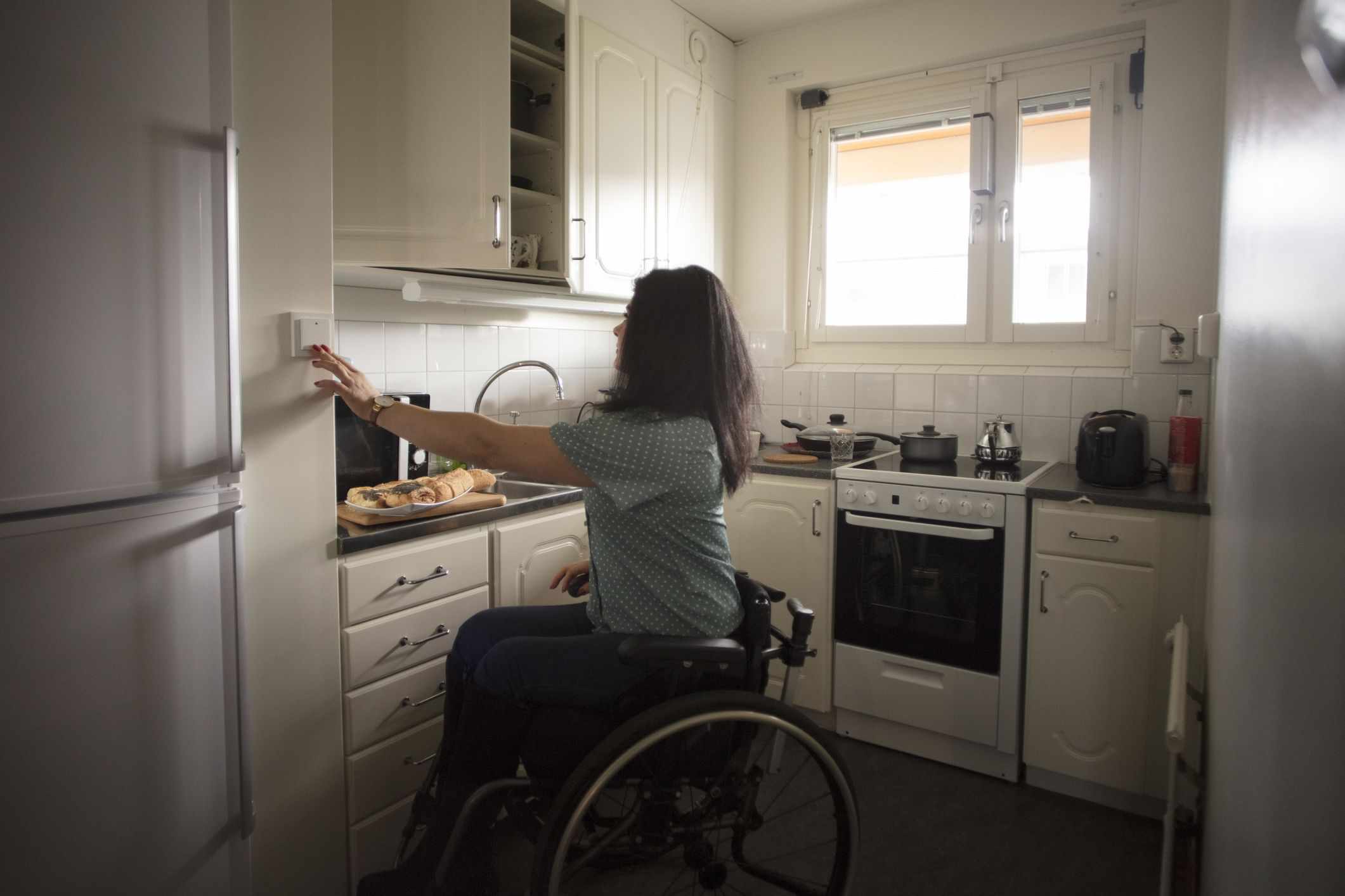 Woman in a Wheelchair Pushing a Button on the Wall in Her Kitchen