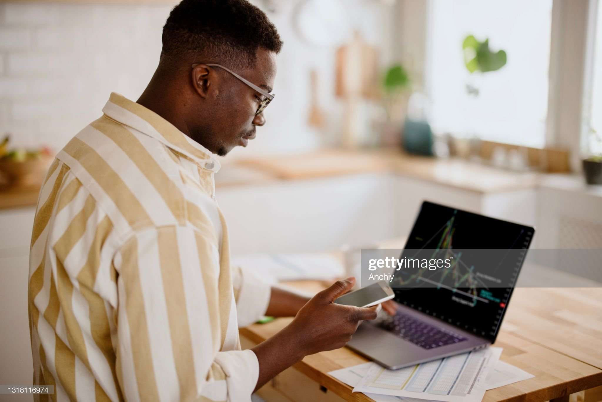 Person at home, checking currency rates with a smartphone and laptop