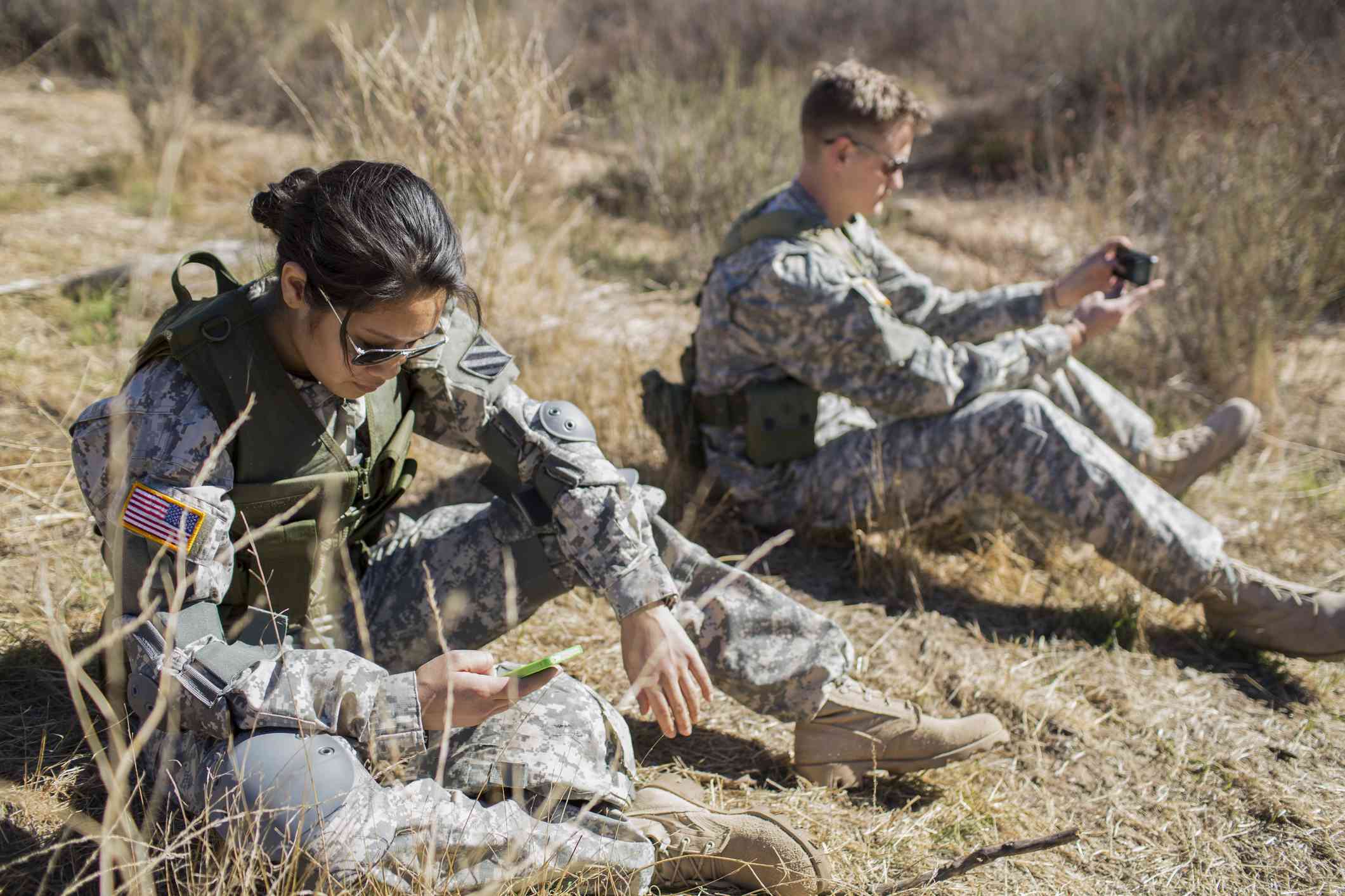 Two active-duty military members using their phones in the field.